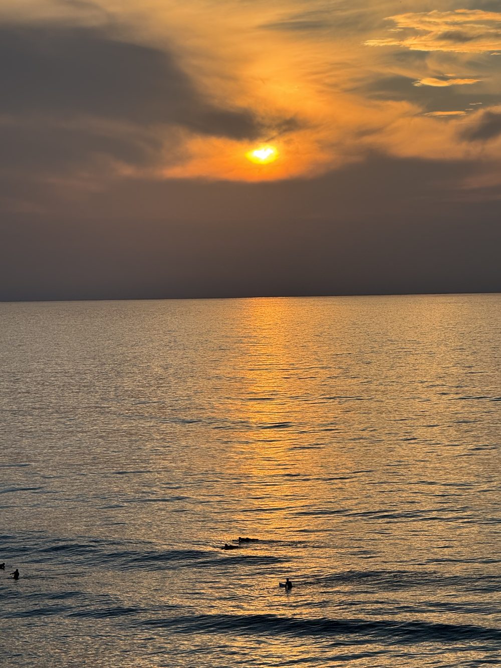 Pôr do sol sobre o mar na Praia de São Julião, Ericeira, com surfistas ao longe